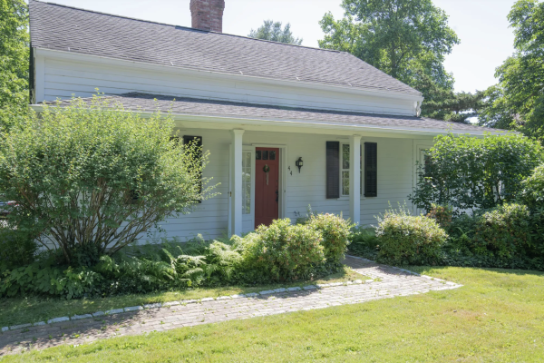 Front view of the historic colonial home at 44 Mountain Rd, Farmington, CT 06032, showcasing a well-maintained garden and a traditional red door under a shaded porch.